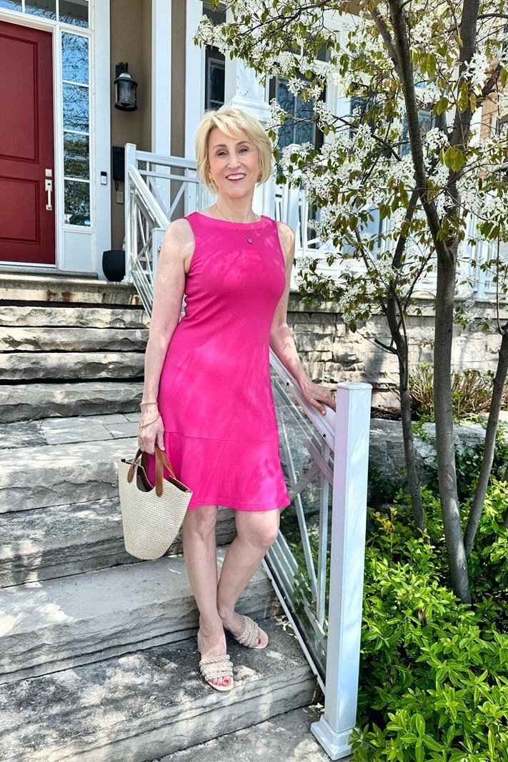 Older woman in a sleeveless hot-pink sheath dress, standing on stone steps - summer dress for women over 50