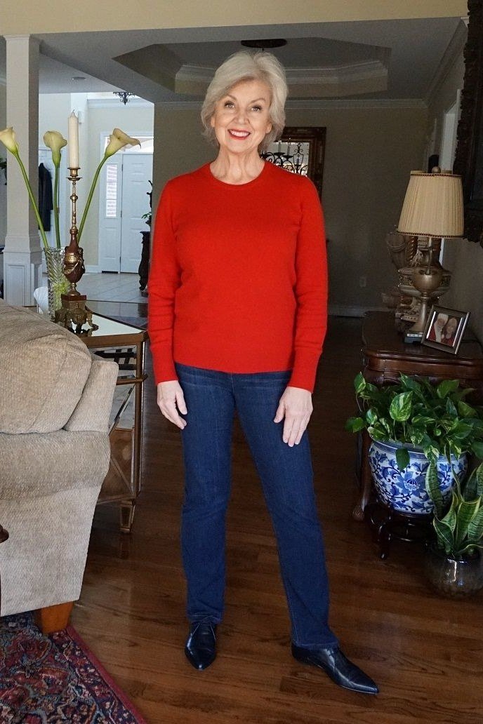 Woman over 60 wearing red sweater, dark jeans, living room