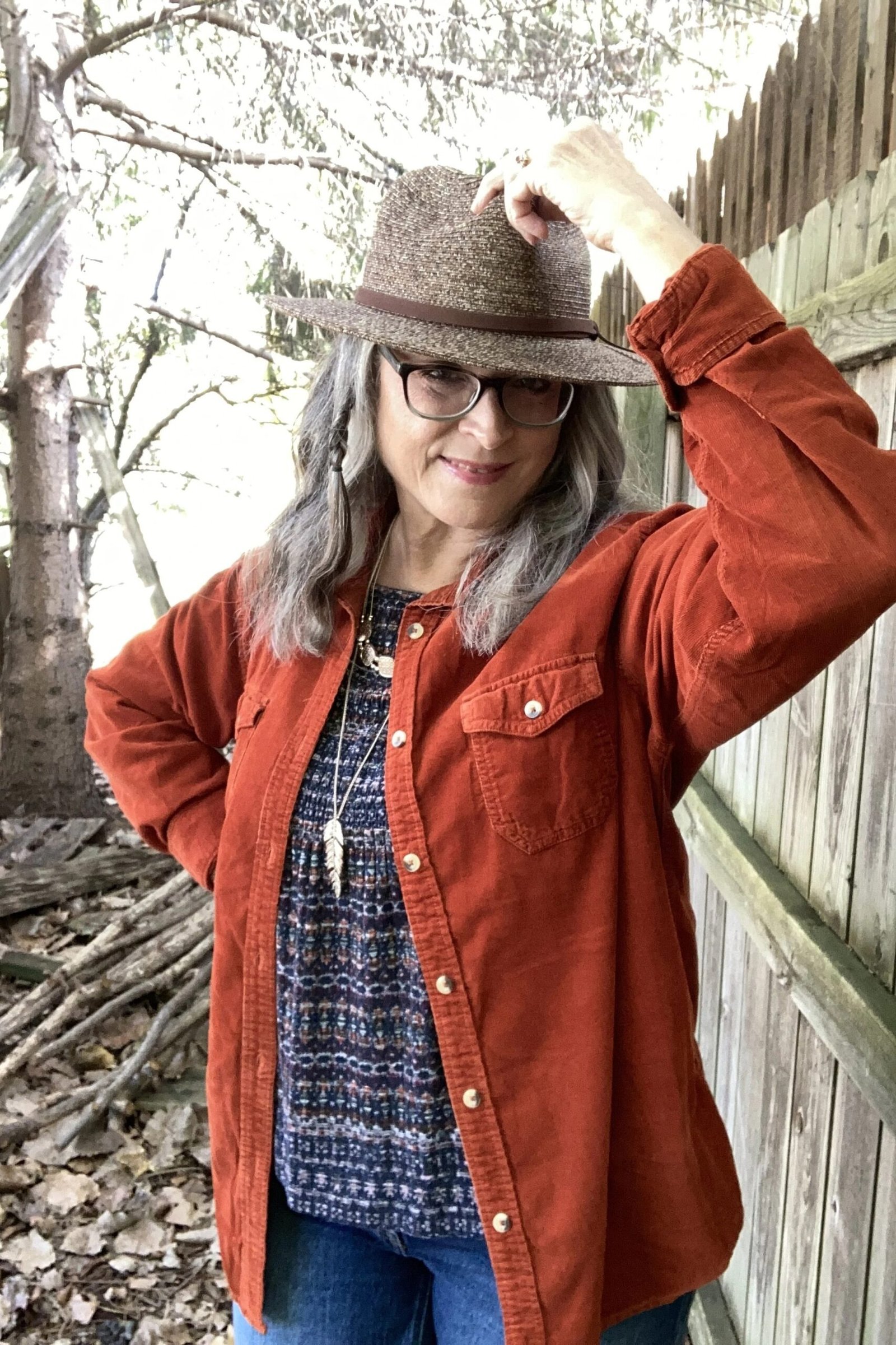 Rust corduroy jacket with patterned blouse, blue jeans and brown felt hat