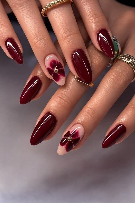 Deep burgundy nails with floral accent and gold rings for women over 50