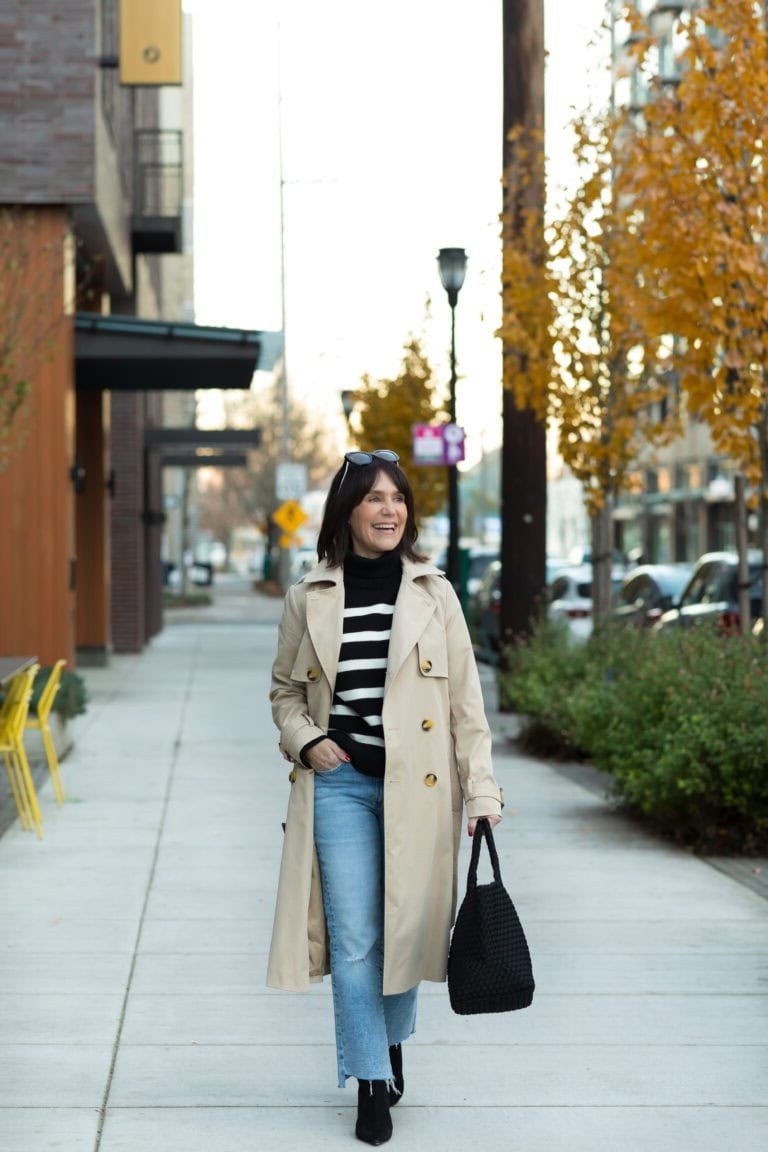 Beige trench coat with striped top light jeans and black bag, casual fall outfit for women over 40