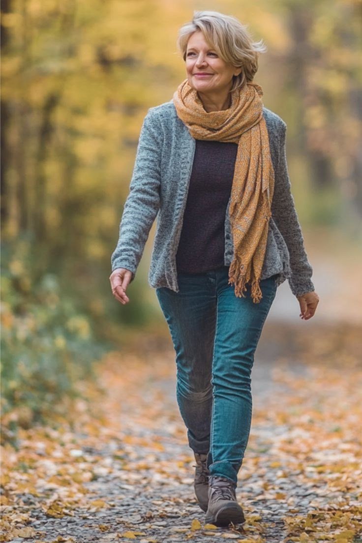 older woman in blue cardigan with mustard scarf and teal jeans, autumn path