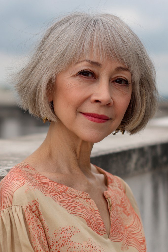 Silver-grey french bob with full bangs and peach blouse