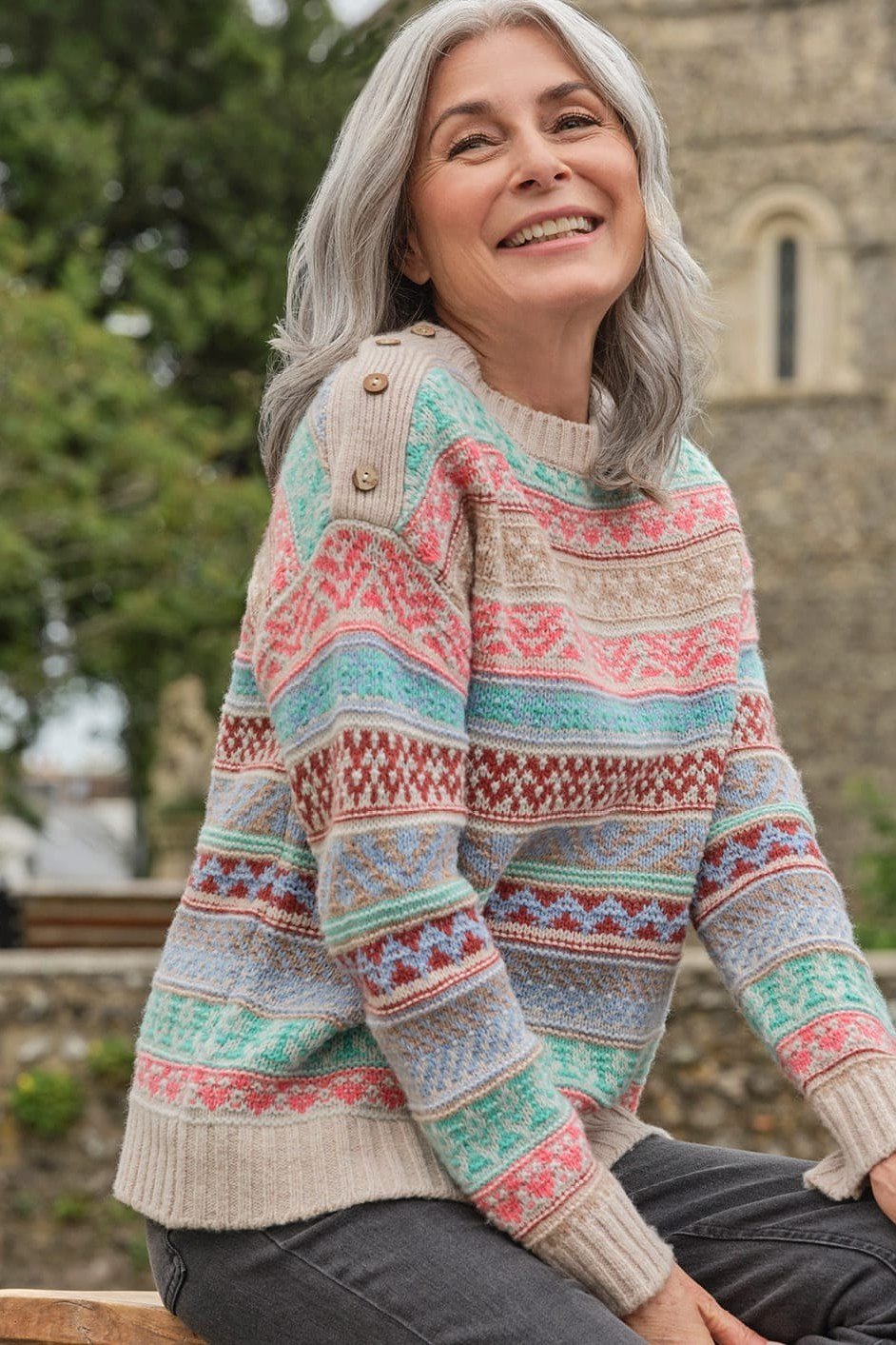 Multicolor fair-isle crew sweater seated by stone church, cozy sweater outfit idea for women over 70