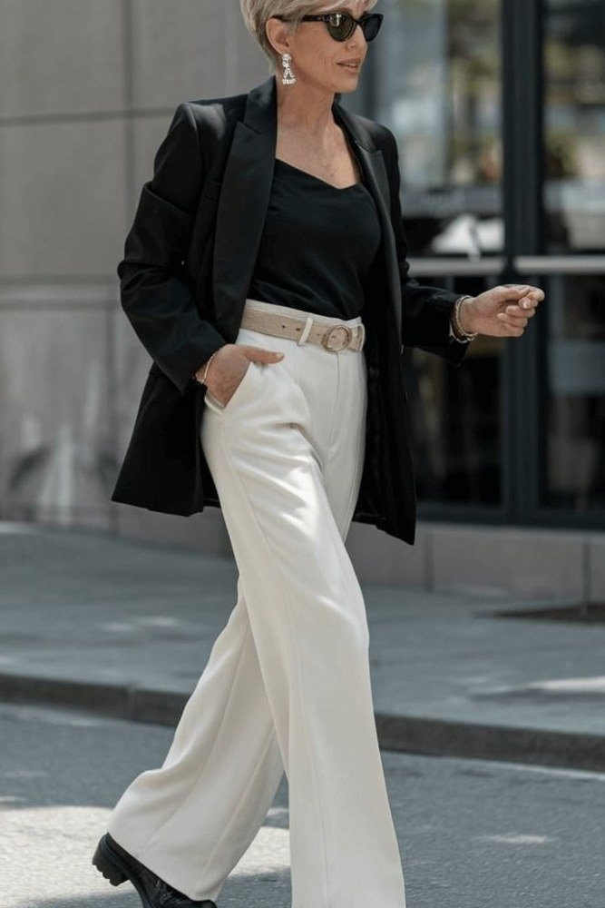 Woman over 60 in a black blazer with a black top and white wide-leg trousers
