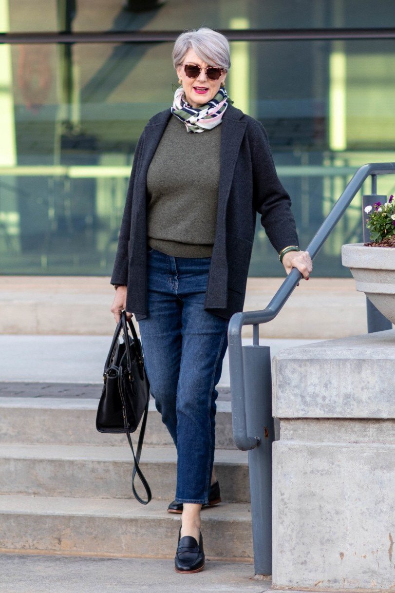 Black coat over olive sweater with blue jeans and black handbag