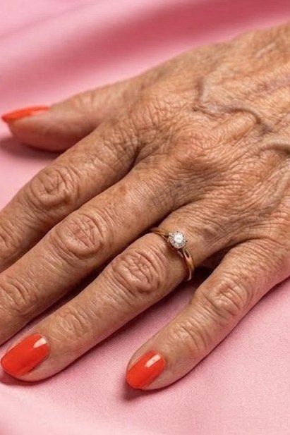 Bright orange glossy nails on elderly hand for women over 70