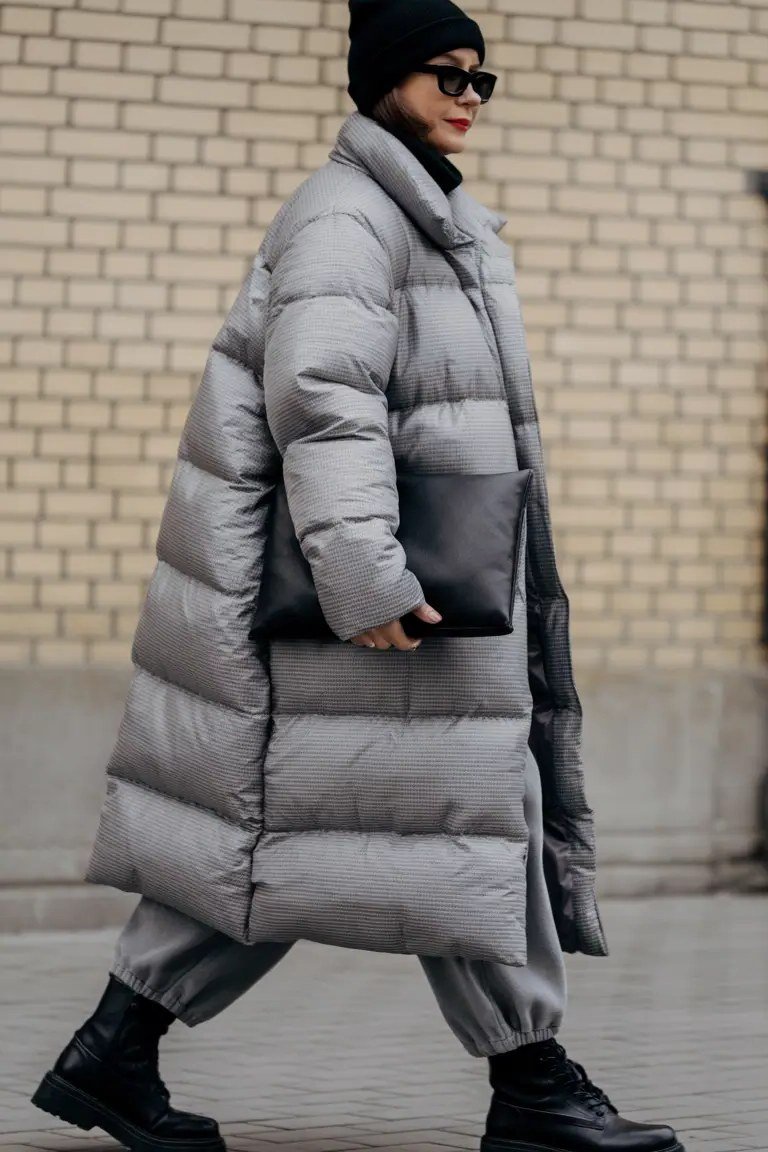 Stylish winter outfit for women over 60: long gray puffer coat with black beanie on a city street