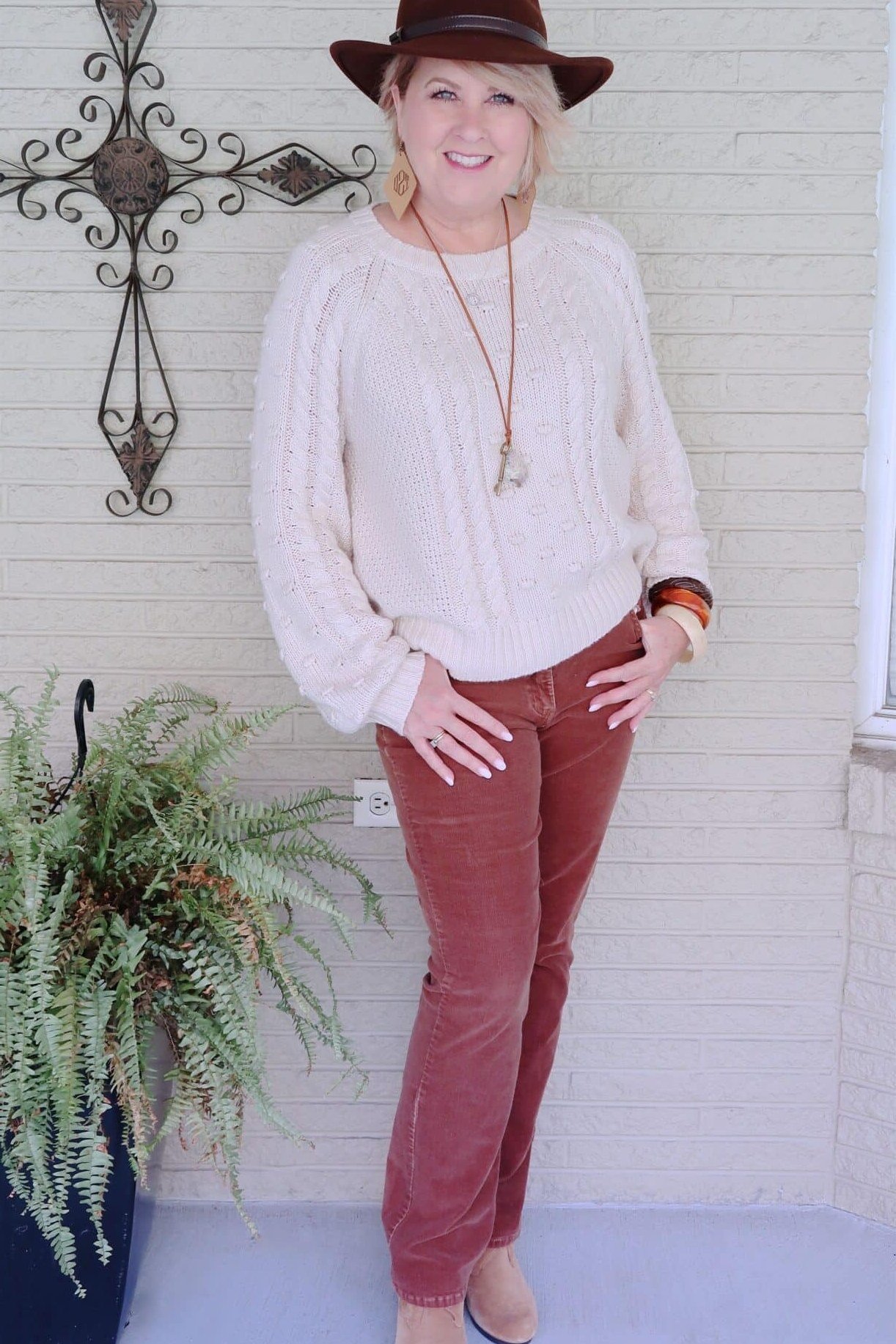 Cream cable knit sweater with rust skinny jeans and brown fedora
