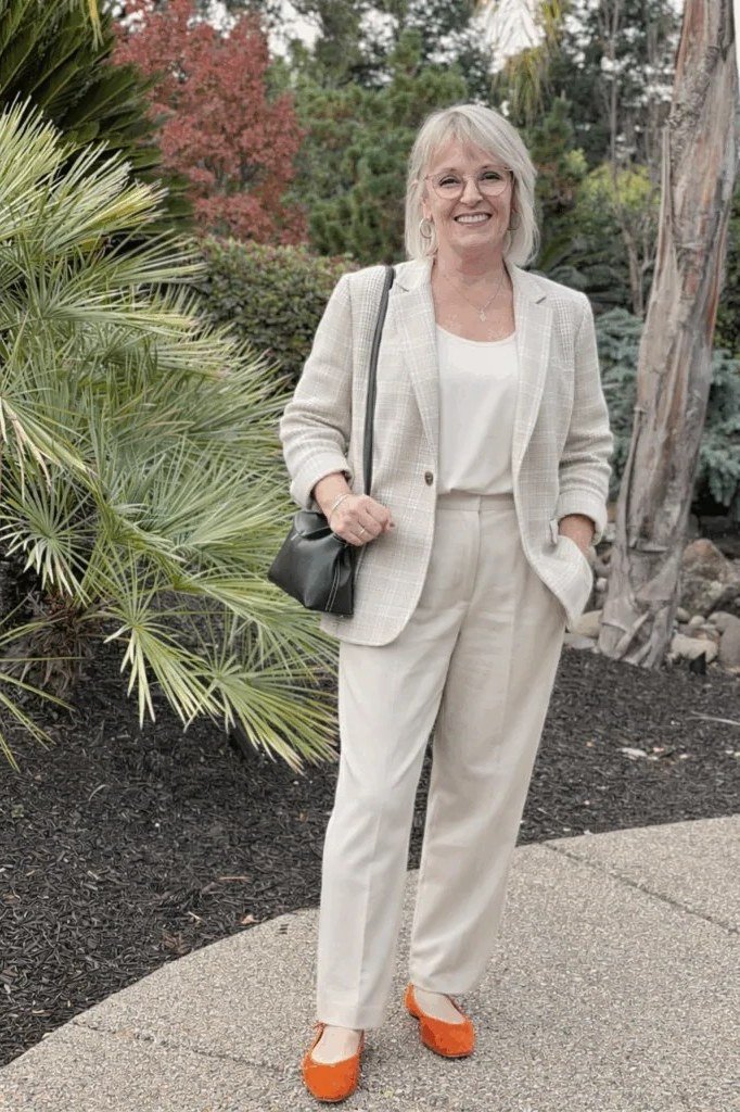 Woman over 50 in a cream monochrome blazer and trousers with orange flats