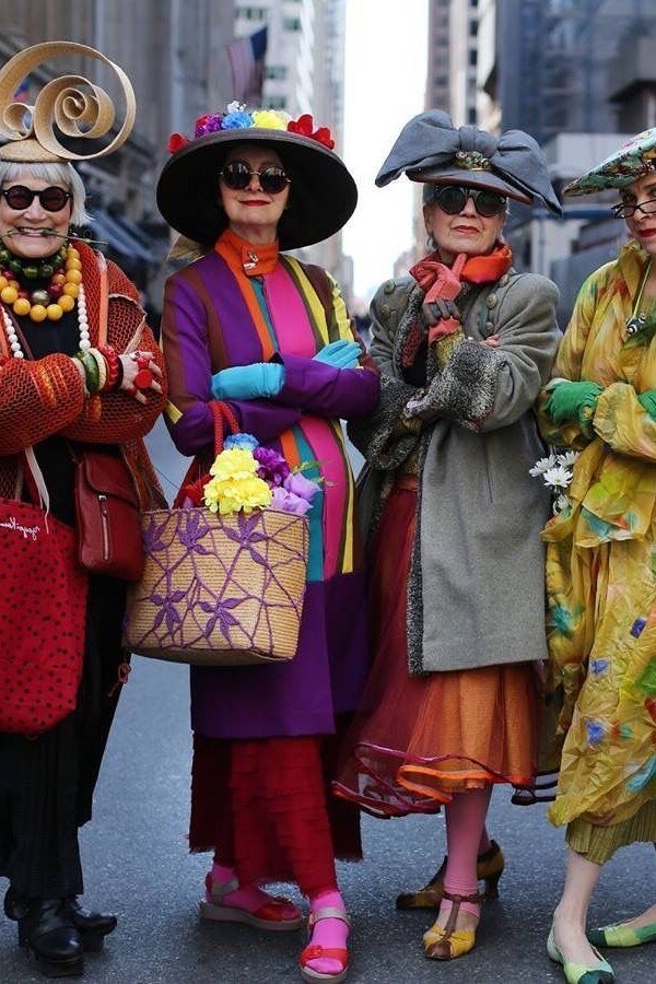 Four eccentric older women in colorful street-style outfits and statement hats posing together in a city - summer dress for women over 50