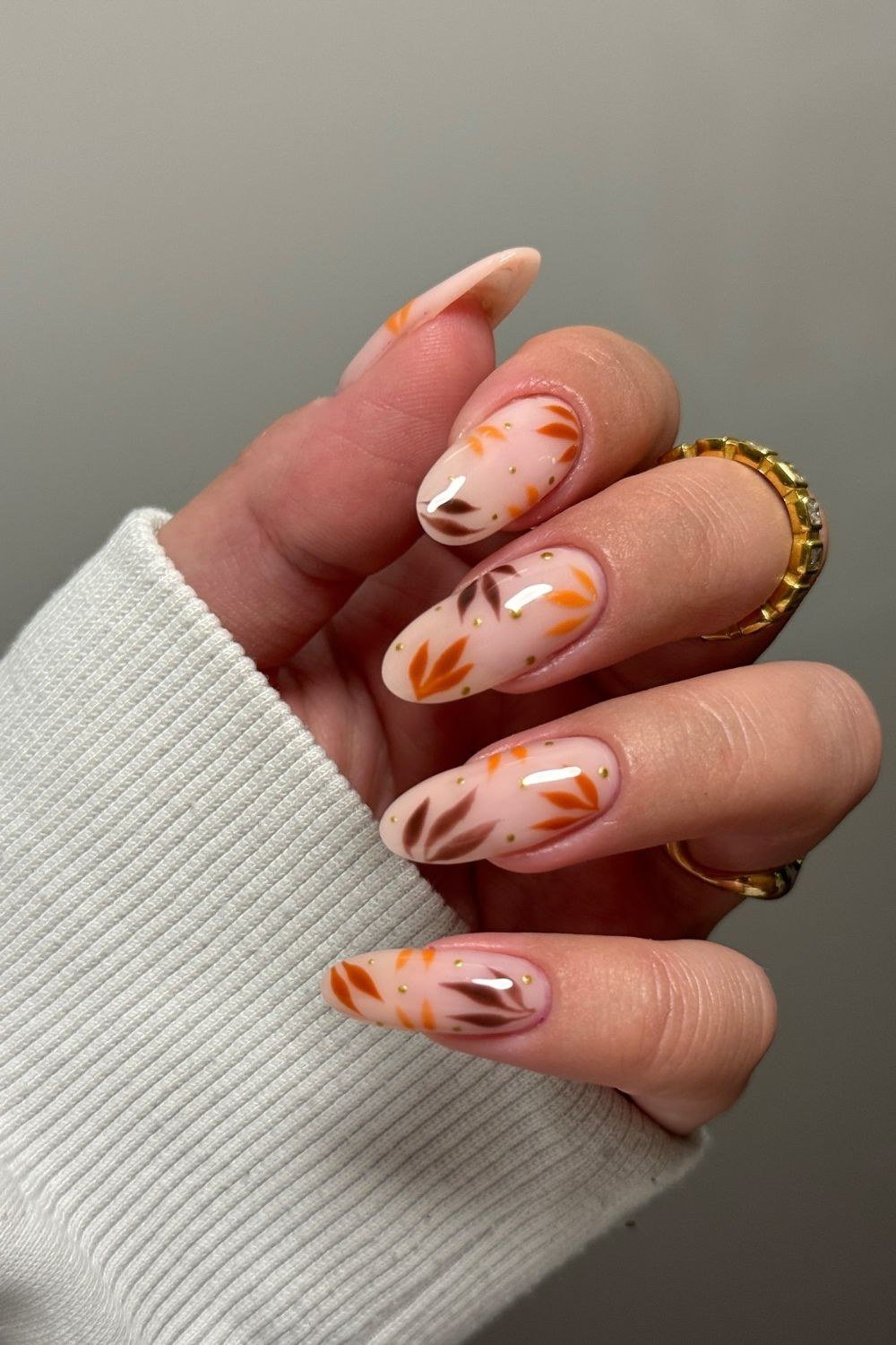 Peach-to-nude ombre with orange autumn leaf art accents, almond shape, medium length, glossy, white sweater cuff, fall nail color for women over 40