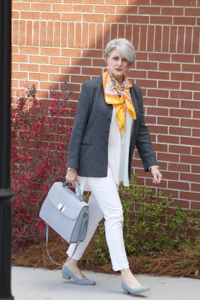 Woman over 50 in a gray blazer with a yellow scarf and white trousers