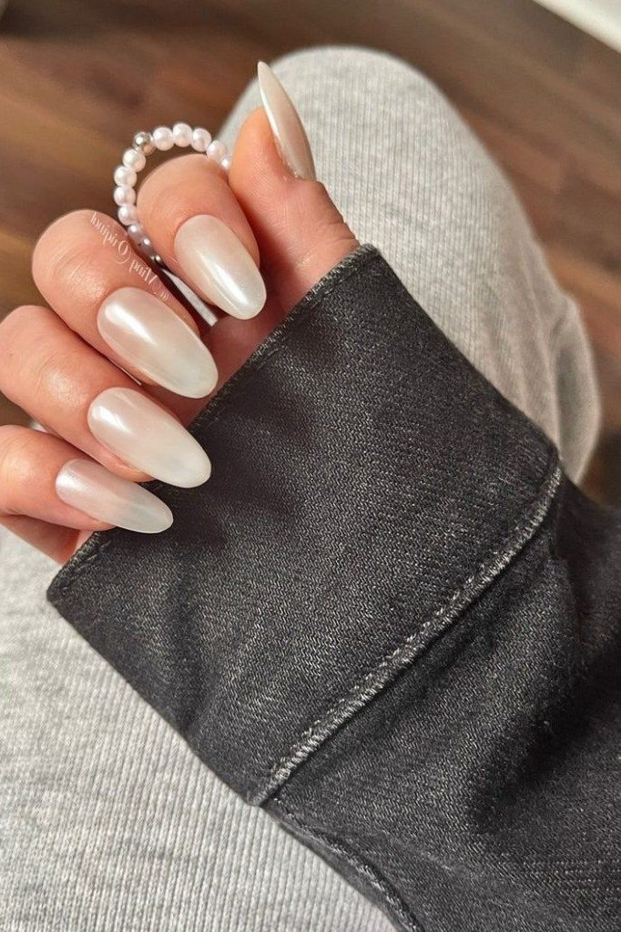 Milky white almond nails styled with a pearl bracelet
