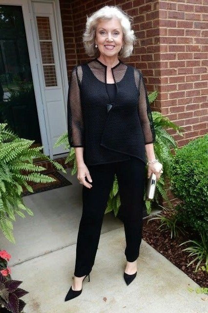 White-haired woman in black sheer-sleeve top with black trousers on porch