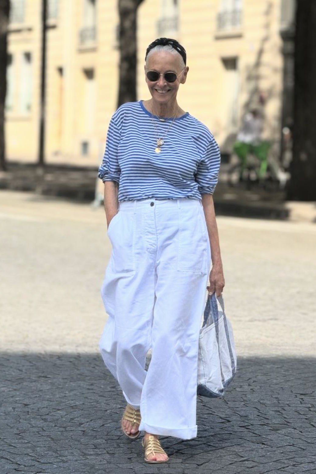 Woman over 50 wearing Blue striped top with white wide-leg pants on a city street.