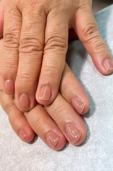 Sheer nude glossy nails on older hands, best manicure idea for women over 60