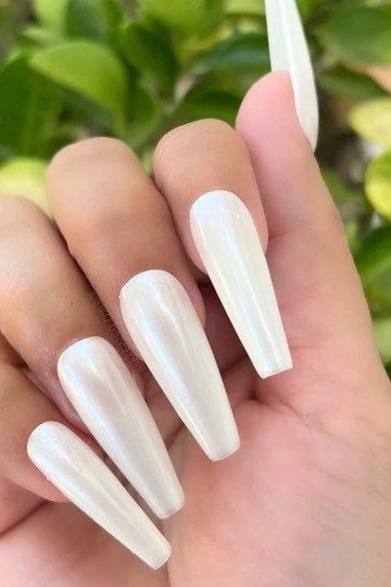 Long milky white nails photographed outdoors with greenery