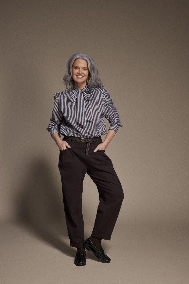 Woman over 60 in a striped shirt with brown high-waist trousers