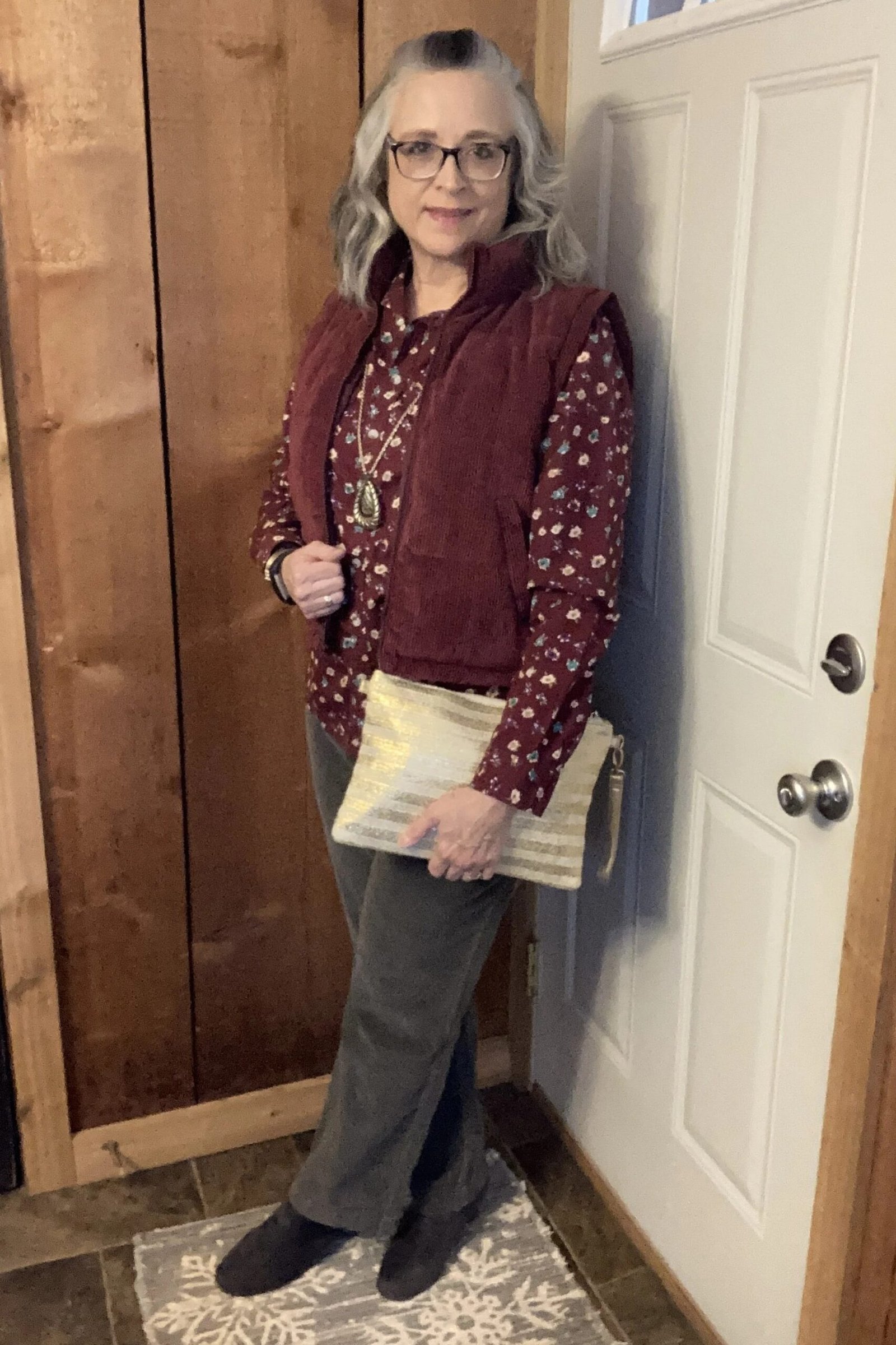 Burgundy quilted vest with patterned blouse and grey trousers