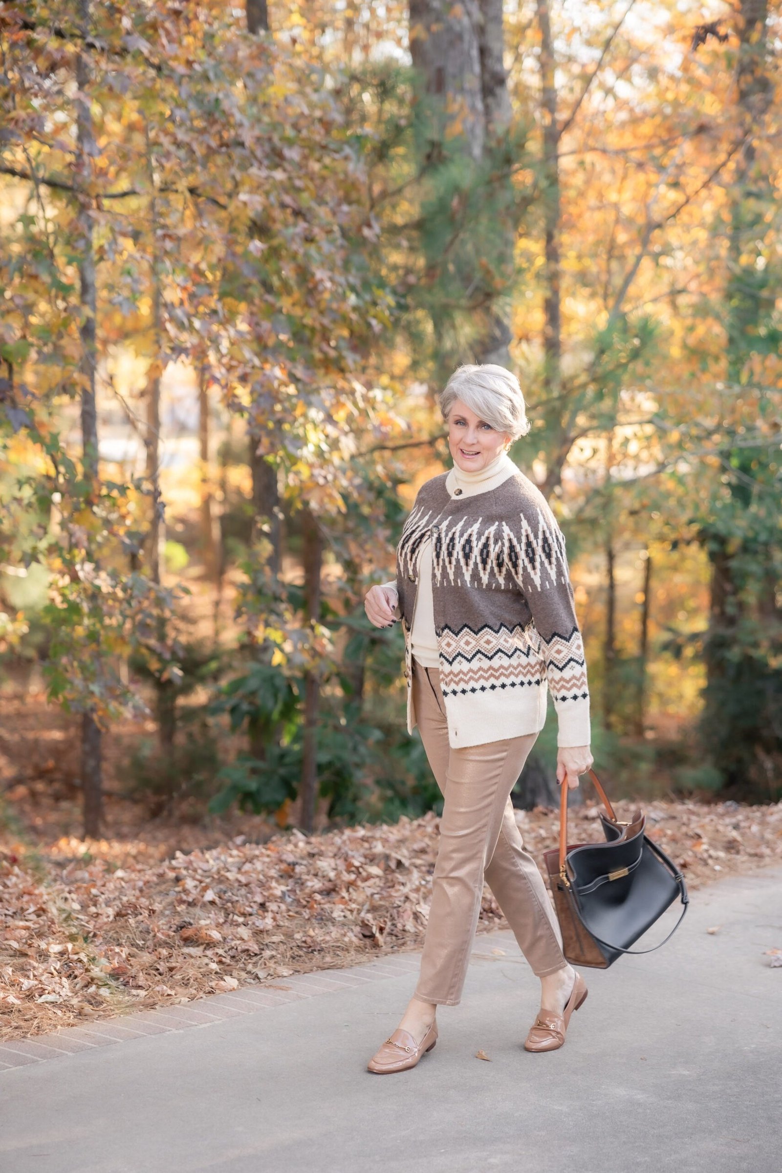 Brown fair-isle tunic sweater with tan trousers walking on path, cozy sweater outfit idea for women over 70