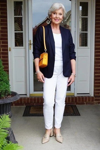 Woman over 50 in a navy blazer with white trousers and a yellow shoulder bag