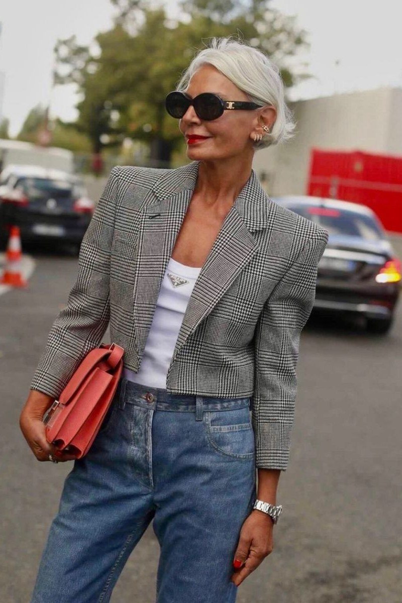 older woman in gray blazer with white top, blue jeans and red clutch