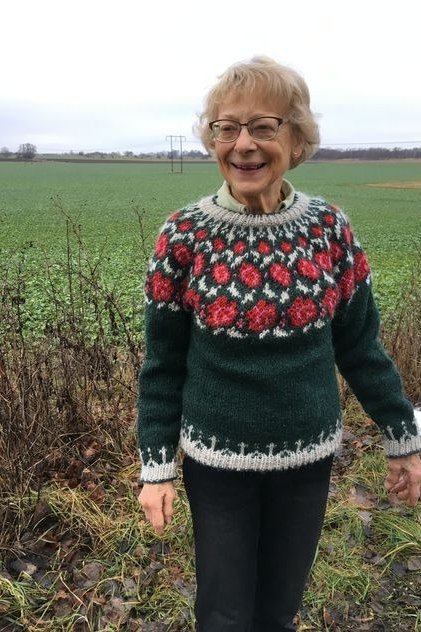 Forest-green rose-pattern fair-isle sweater standing in a field, cozy sweater outfit idea for women over 70