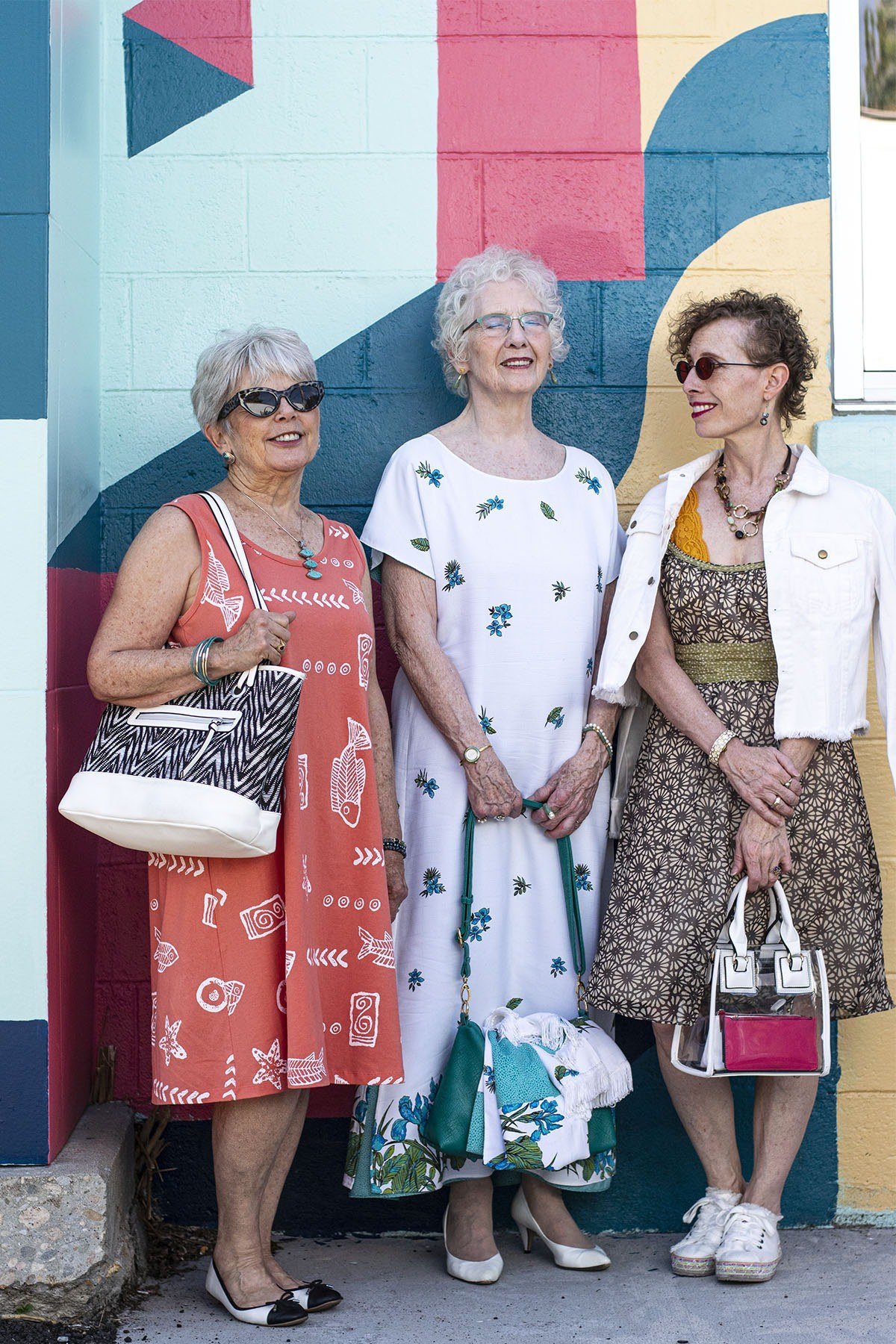 Three women in floral and patterned summer dresses posing in front of a colorful mural - summer dress for women over 50