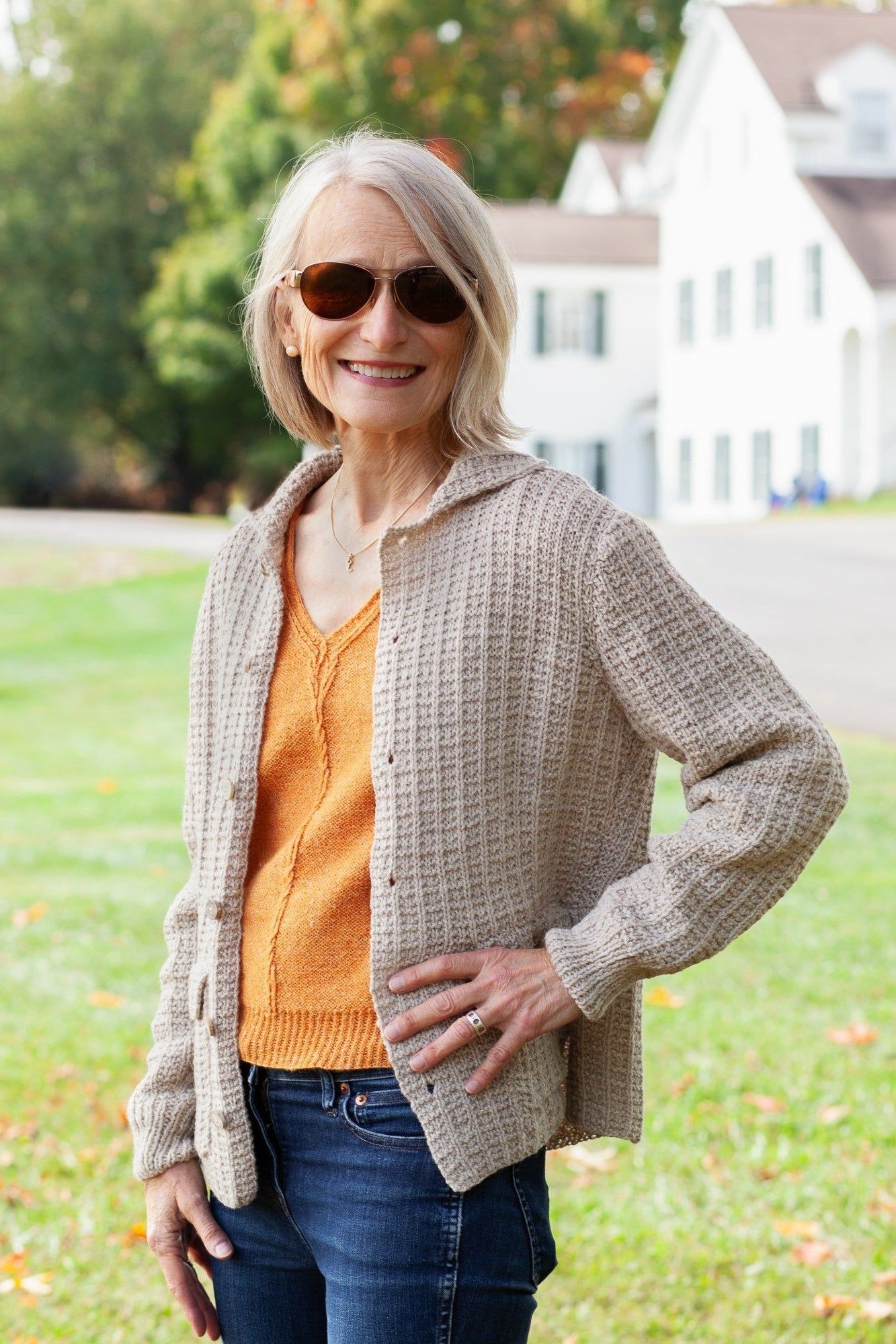 Beige knit cardigan over orange top with blue jeans, woman over 50