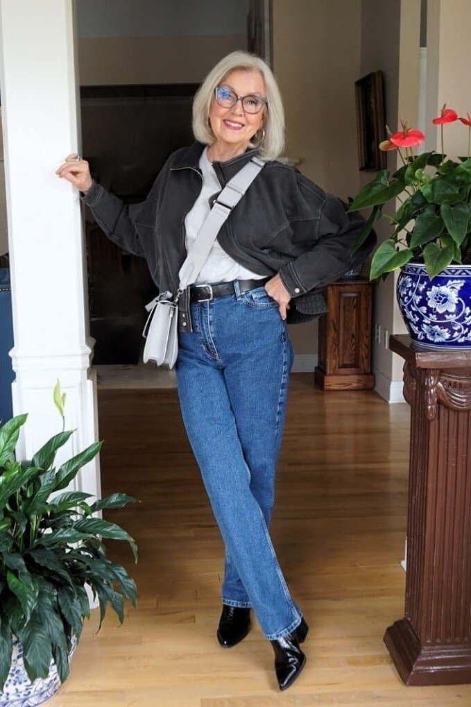 Woman over 60 wearing black jacket, white tee, medium jeans, black heels, doorway