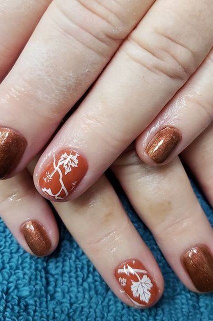 Copper burnt orange with white leaf art accents, short oval, glossy, mature hands, teal towel background, fall nail color for women over 40