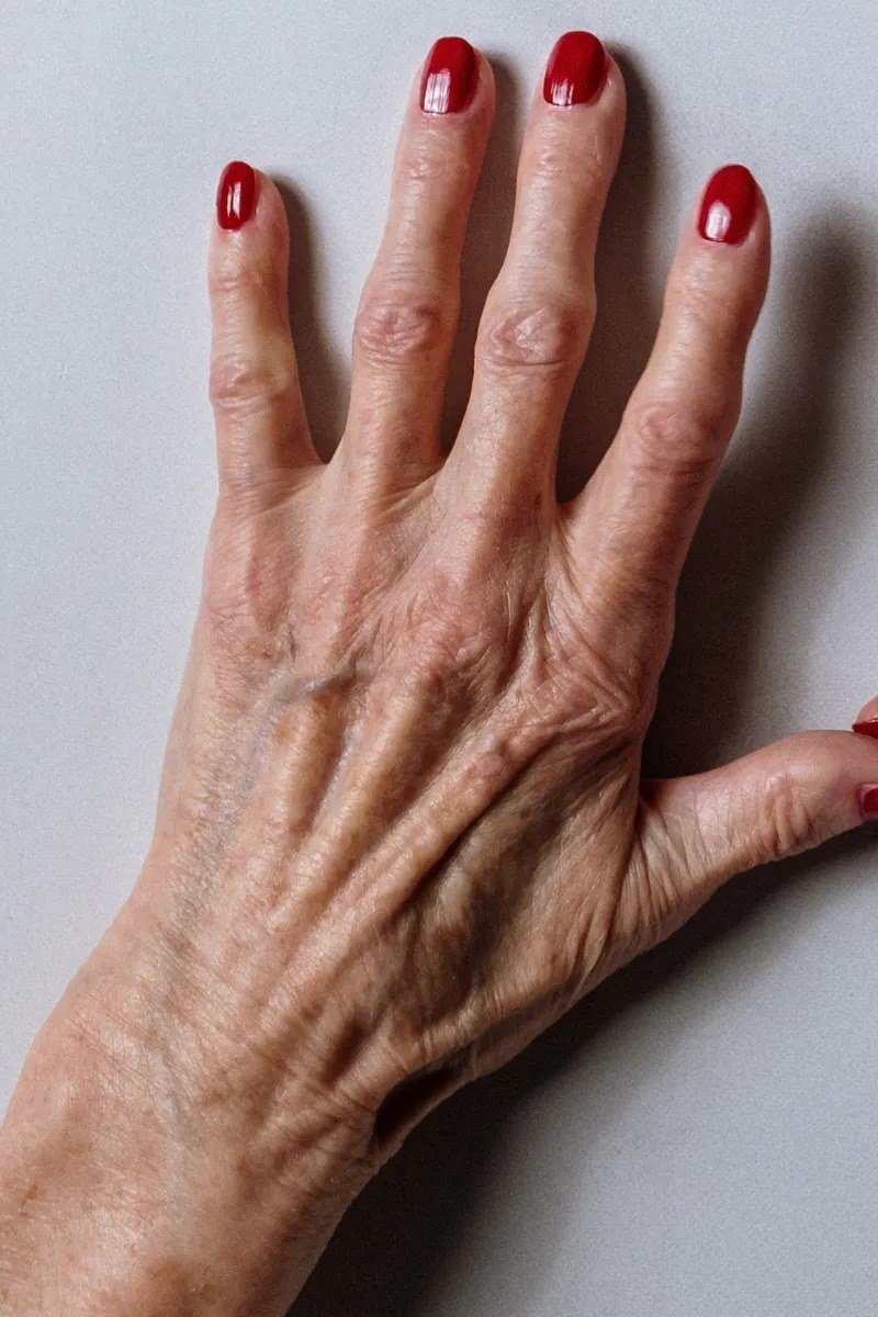 Deep red short almond nails on elderly hand