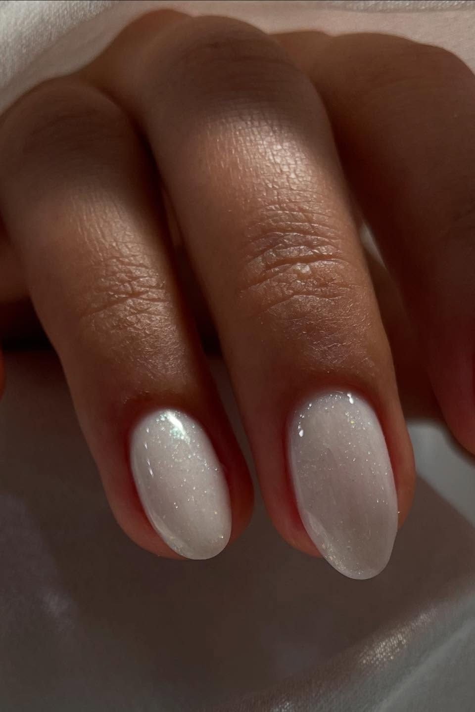 Chrome milky white nails glowing on dark skin close up