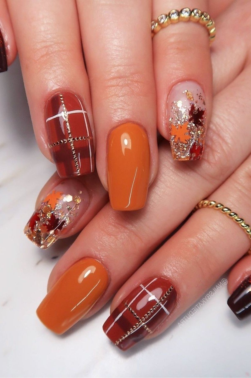 Bright orange short nails with plaid and autumn leaf nail art, glossy fall pattern.