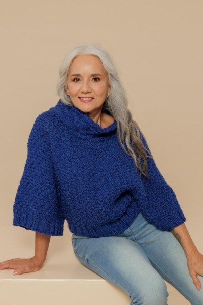 Cobalt-blue cowl-neck sweater with jeans seated on bench, cozy sweater outfit idea for women over 70