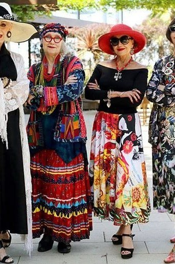 Four stylish women in colorful patterned summer dresses and hats posing outdoors - summer dress for women over 50