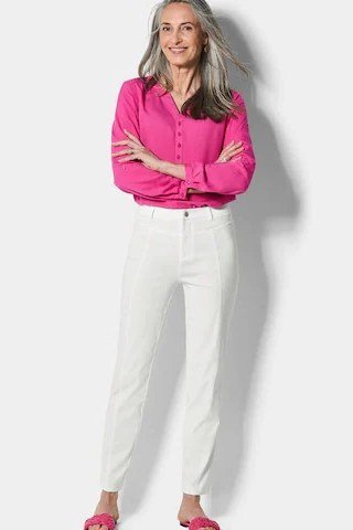 Woman over 60 in a hot pink shirt with white jeans and pink flats