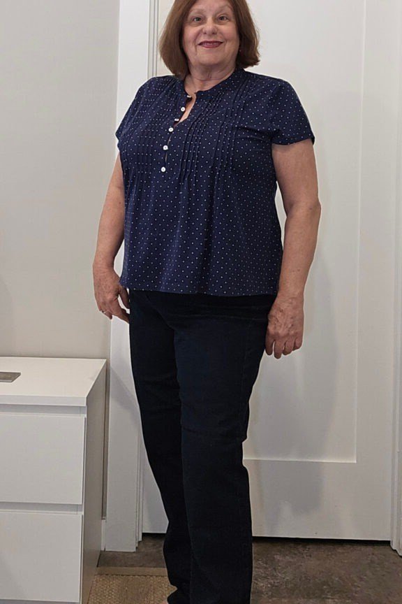 Woman over 60 wearing navy polka-dot top, dark jeans, red shoes, indoors