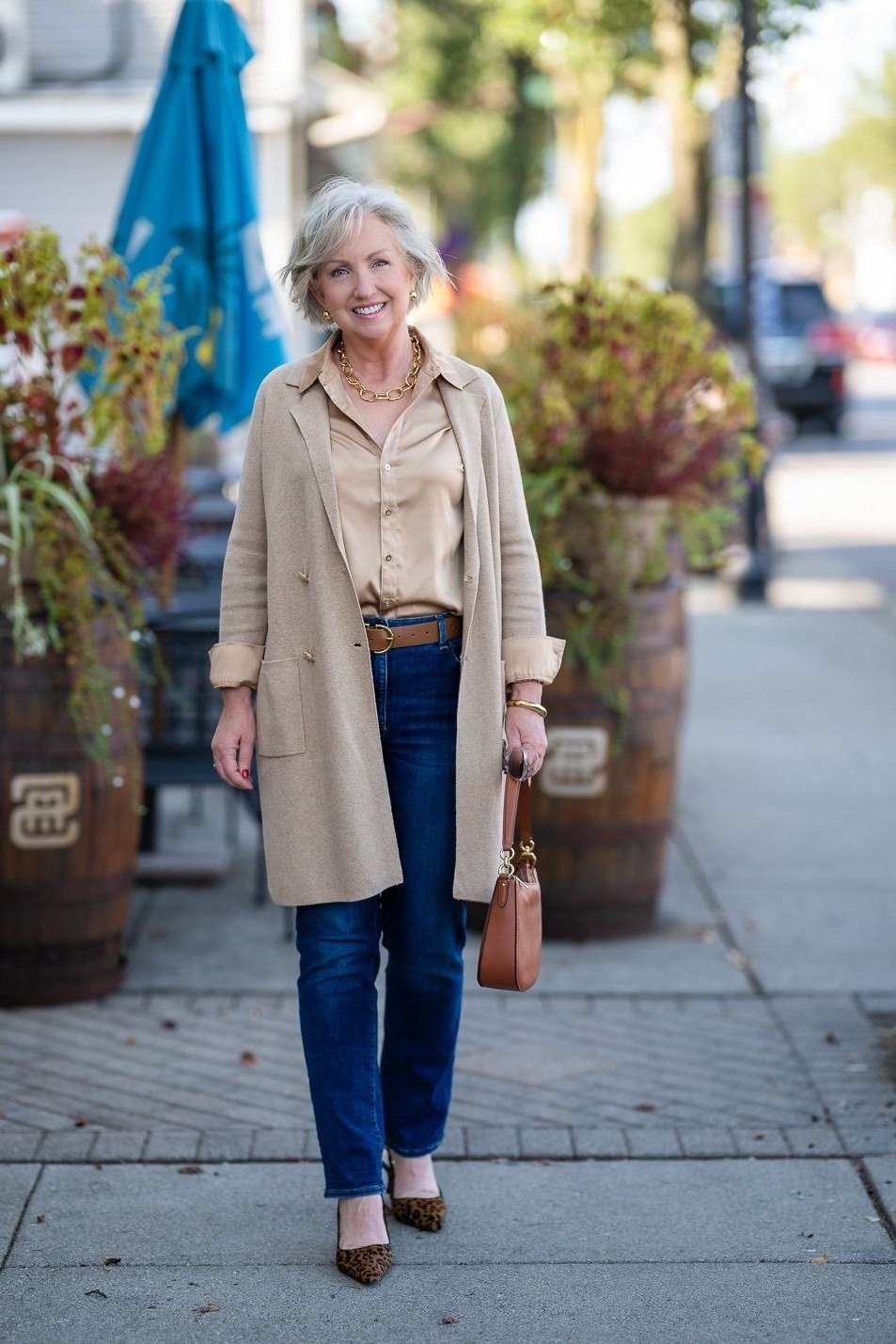 Long beige cardigan with tan shirt and blue jeans on sidewalk