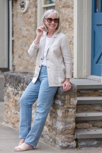 Woman over 60 wearing beige blazer, light jeans, stone building