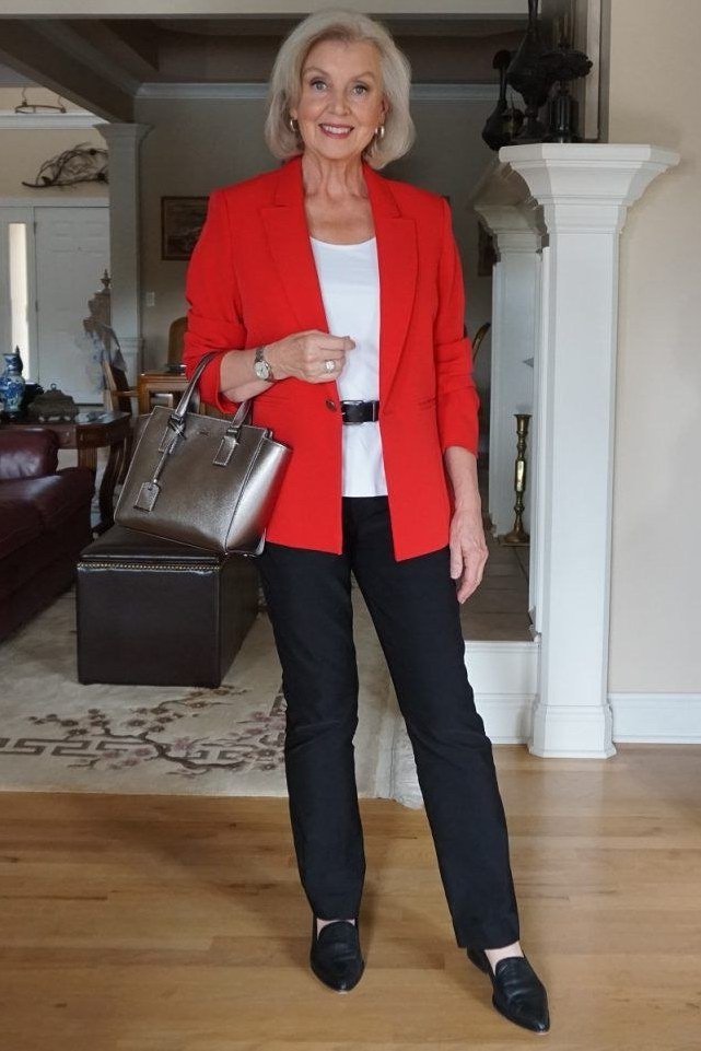 Woman over 50 in a red blazer with gray trousers and a silver tote