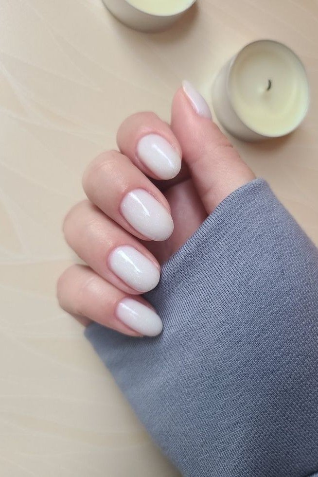 Short milky white nails styled beside glowing candles