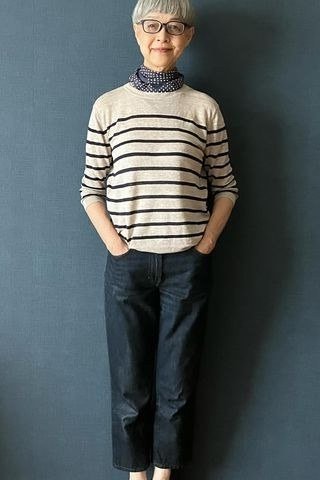 Woman over 60 wearing striped turtleneck sweater, dark jeans, teal wall