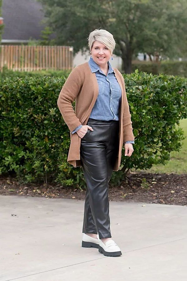 Fall city outfit for women over 50: camel coat blue shirt black leather pants white sneakers