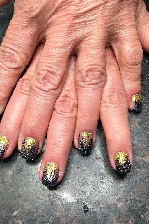 Nail art design for women over 60: black and gold glitter nails on older hands