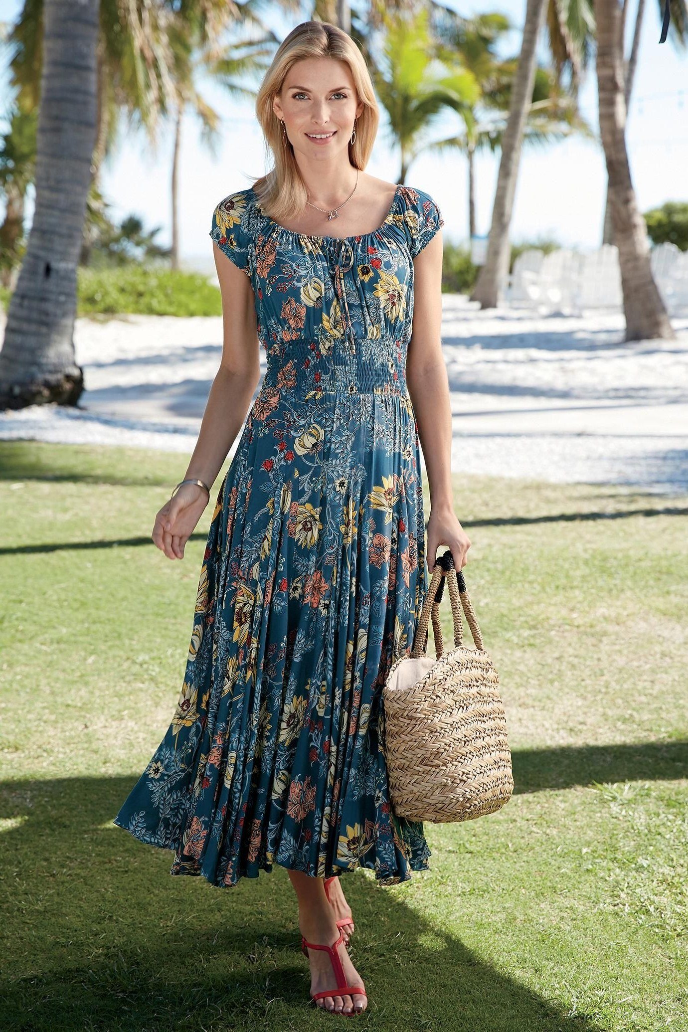 Woman in a blue-and-green patterned sleeveless maxi dress with a straw tote, sunny lawn - summer dress for women over 50