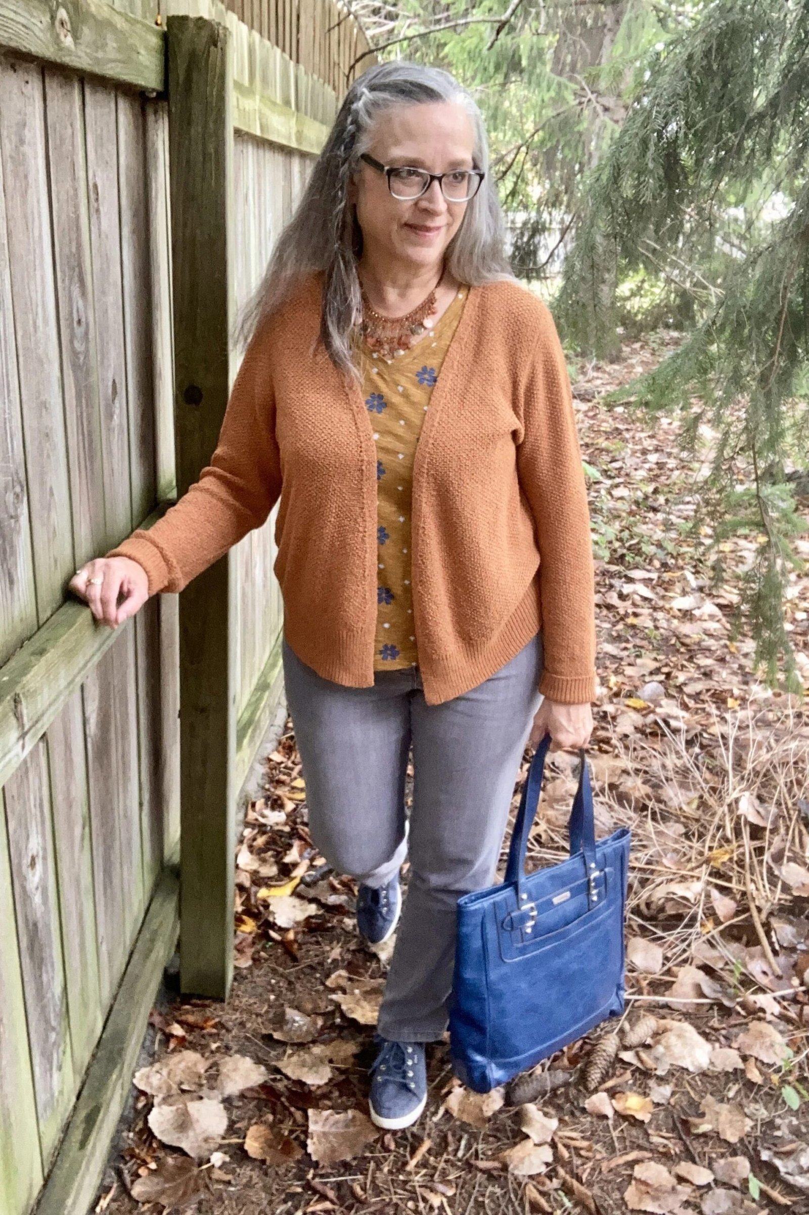 Camel open cardigan over floral blouse with gray jeans and blue handbag