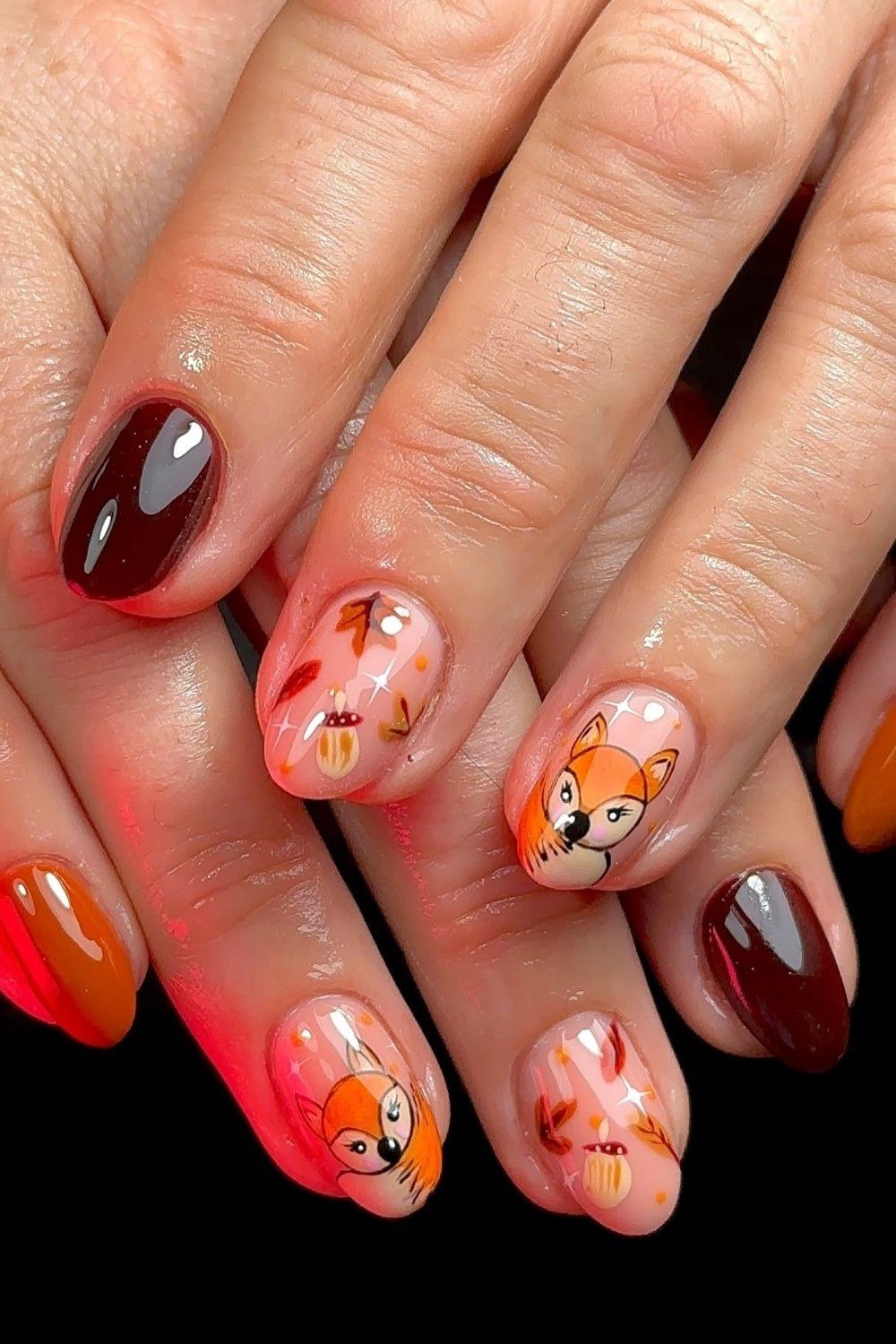 Burgundy almond nails with a cute fox and autumn leaf nail art on a black background.
