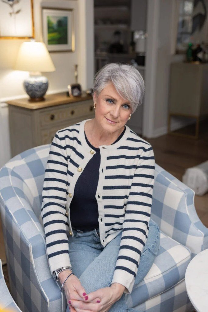 Woman over 50 wearing Striped cardigan with navy top and jeans, seated in an armchair.